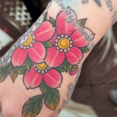 Tatuaje colorido de flores rosas con hojas verdes en la muñeca de una persona.